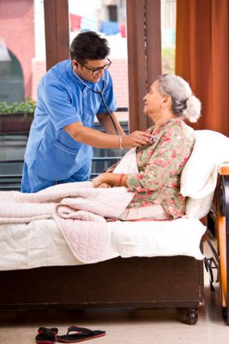 Home caregiver examining senior woman using stethoscope on bed